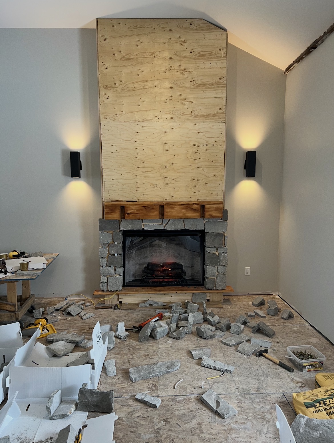 Stone fireplace with masonry and wall sconce lighting during basement renovation by Inline Electric